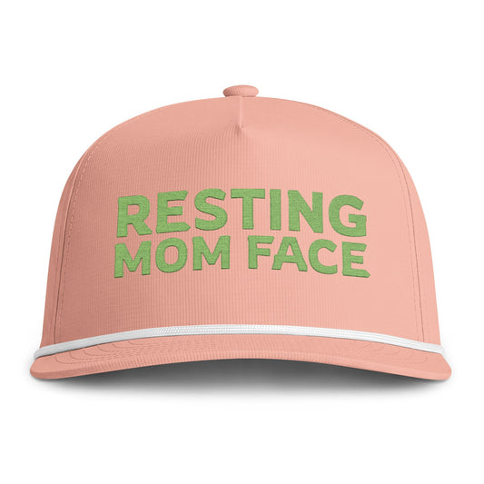 Image of a peach hat with green embroidery reading "Resting Mom Face"