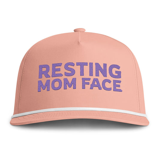 Image of a peach hat with purple embroidery reading "Resting Mom Face"