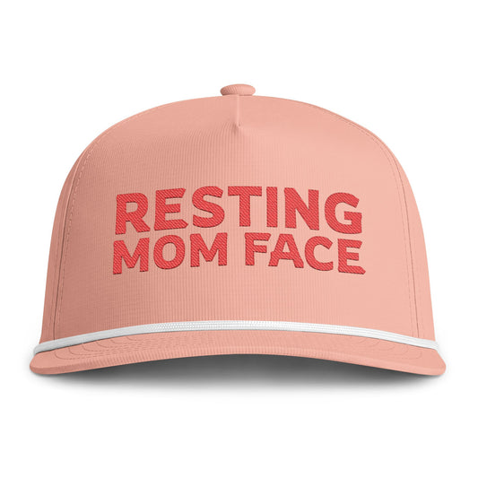 Image of a peach hat with red embroidery reading "Resting Mom Face"
